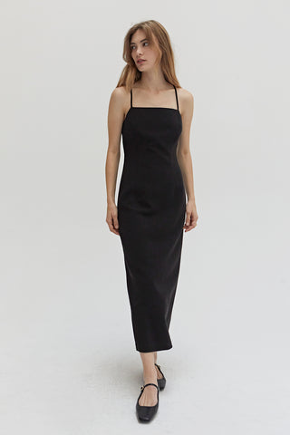 A woman wearing a black midi dress with criss cross back strap detail.