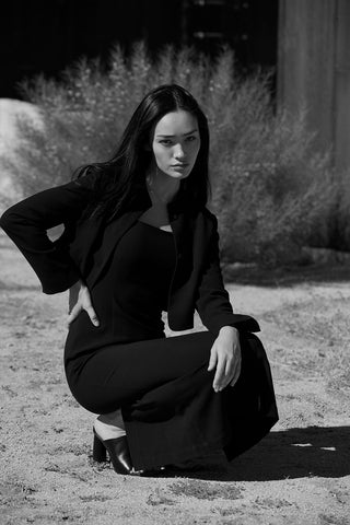 A woman wearing a black midi dress with criss cross back strap detail.