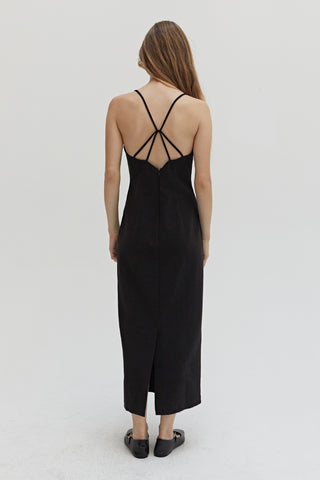 A woman wearing a black midi dress with criss cross back strap detail.