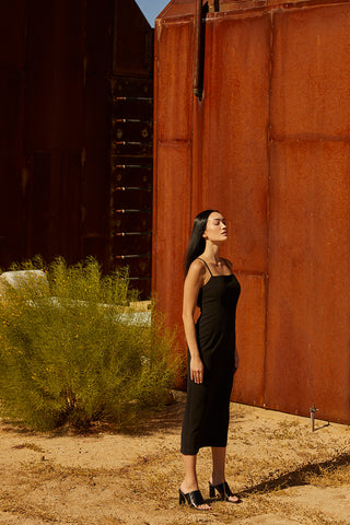 A woman wearing a black midi dress with criss cross back strap detail.