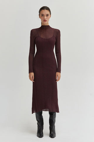 A woman wearing a sheer lurex knit mock neck maxi dress with long sleeves.