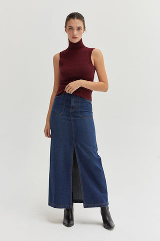 A woman wearing a high waisted denim maxi skirt with front center slit.