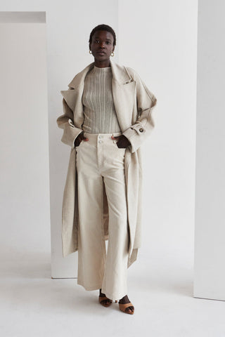a model wearing a long beige coat with a beige high-neck top and pants
