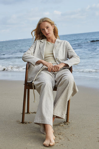 a model sitting on the beach in a pinstripe blazer set