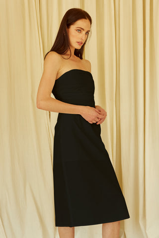 A woman wearing a black ruched bodice straight line midi dress.