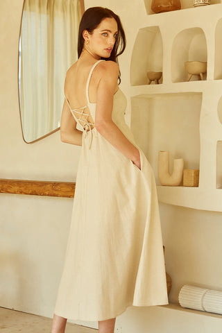 A woman wearing an oatmeal corset back midi linen dress.