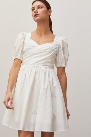 A woman wearing an ivory pleated front mini dress.
