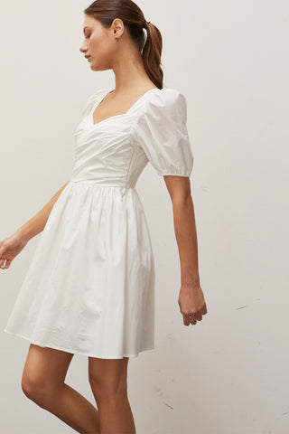 A woman wearing an ivory pleated front mini dress.