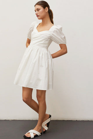 A woman wearing an ivory pleated front mini dress.