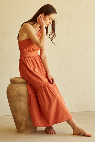 A woman wearing a rust one-shoulder midi dress.