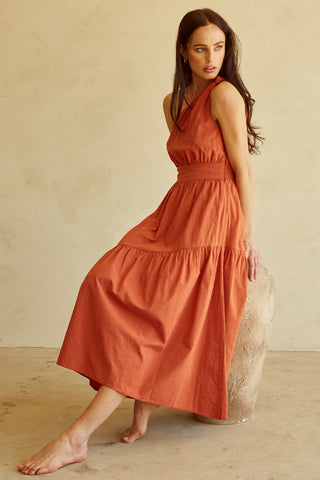 A woman wearing a rust one-shoulder midi dress.