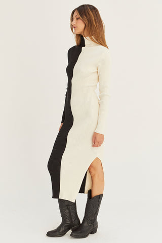 A model wearing a black/cream color block turtle neck midi sweater dress.