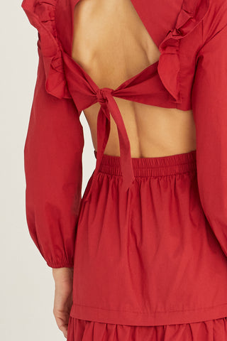 A woman wearing an oxblood tiered poplin maxi dress with back cut out details.