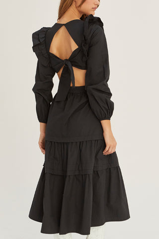 A woman wearing a black tiered poplin maxi dress with back cut out details.