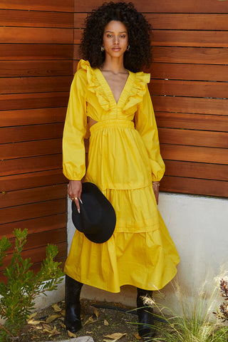 A woman wearing a marigold tiered poplin maxi dress with back cut out details.