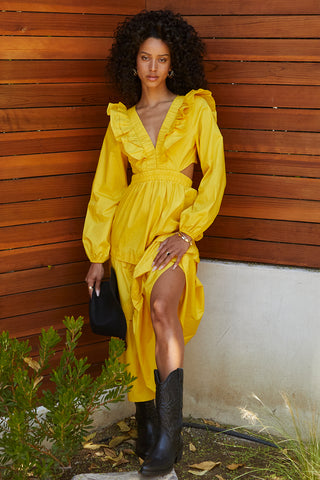 A woman wearing a marigold tiered poplin maxi dress with back cut out details.