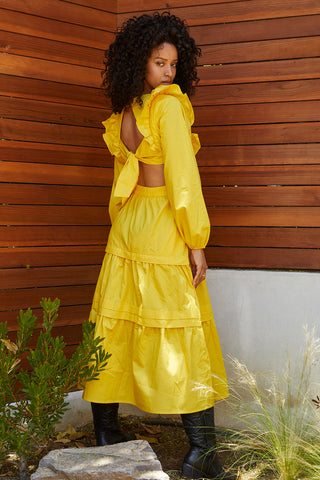 A woman wearing a marigold tiered poplin maxi dress with back cut out details.