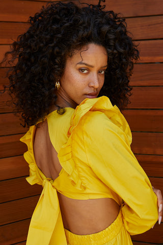 A woman wearing a marigold tiered poplin maxi dress with back cut out details.