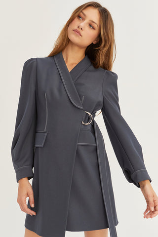 A model wearing a slate blazer surplice mini dress with D-ring buckle detail on front.