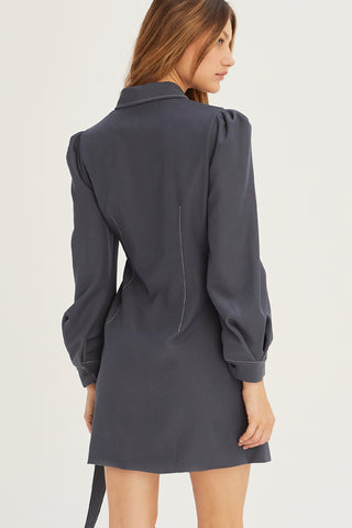 A model wearing a slate blazer surplice mini dress with D-ring buckle detail on front.