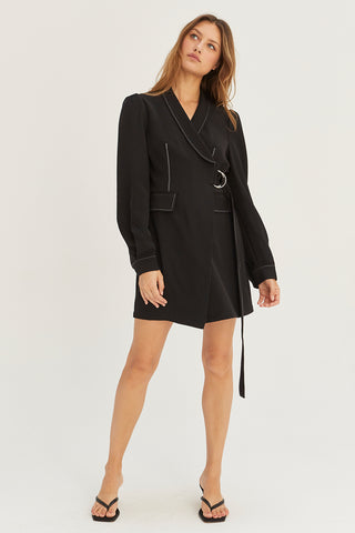 A model wearing a black blazer surplice mini dress with D-ring buckle detail on front.