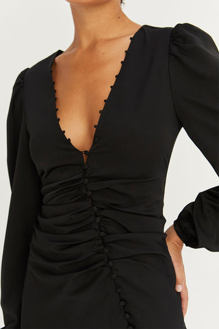 A model wearing a black satin balloon sleeve dress with asymmetric front button detail.