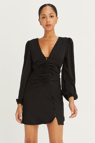 A model wearing a black satin balloon sleeve dress with asymmetric front button detail.