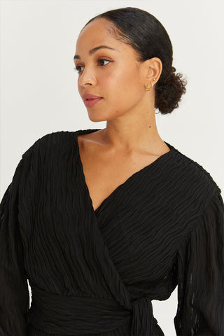 A model wearing a black pleated chiffon wrap mini dress.