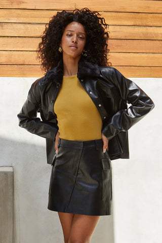 A model wearing a black vegan leather jacket with detachable fur collar.