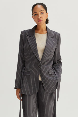 A model wearing a grey pinstriped blazer with waist belt.