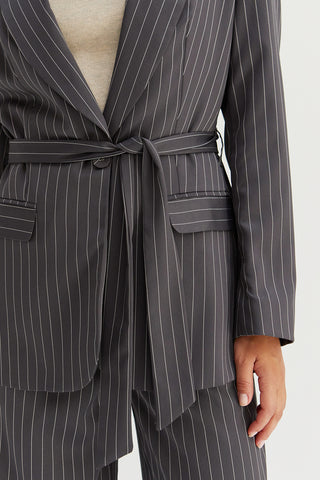 A model wearing a grey pinstriped blazer with waist belt.
