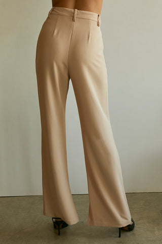 A model wearing a tan wide-leg trousers with slits at inseam hem.
