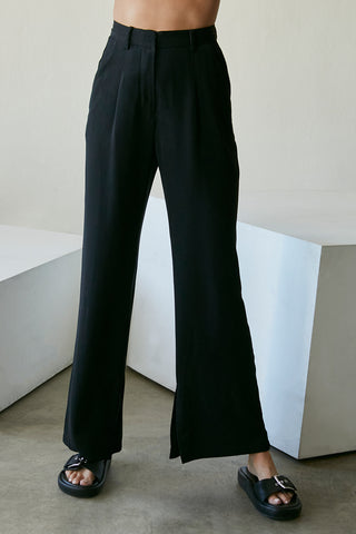 A model wearing a black wide-leg trousers with slits at inseam hem.