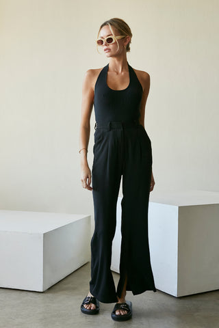 A model wearing a black wide-leg trousers with slits at inseam hem.
