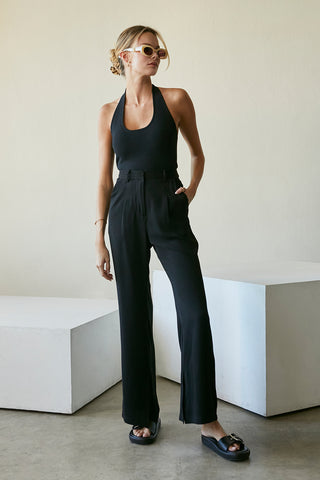 A model wearing a black wide-leg trousers with slits at inseam hem.