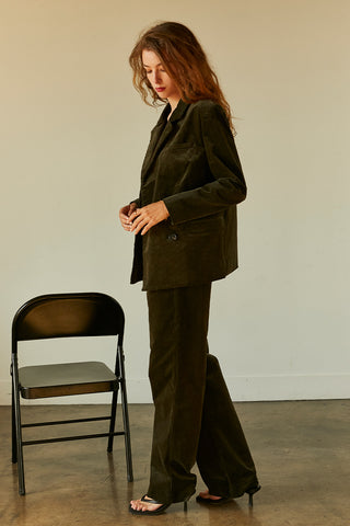 A woman wearing a dark green corduroy trousers with matching corduroy blazer.