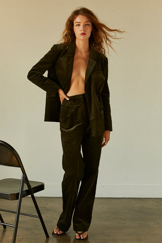 A woman wearing a dark green corduroy trousers with matching corduroy blazer.