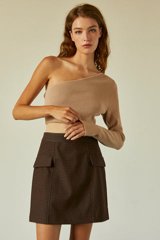 A woman wearing a beige one shoulder long sleeve cropped top.