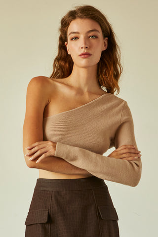 A woman wearing a beige one shoulder long sleeve cropped top.