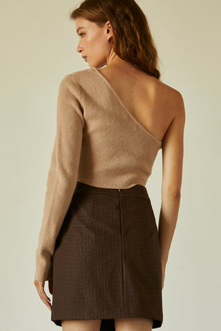A woman wearing a beige one shoulder long sleeve cropped top.