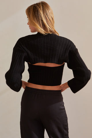 A model wearing a black stretchy knit bolero set.