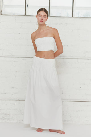 A woman wearing an ivory all-over smoked tube top and maxi skirt two piece set.