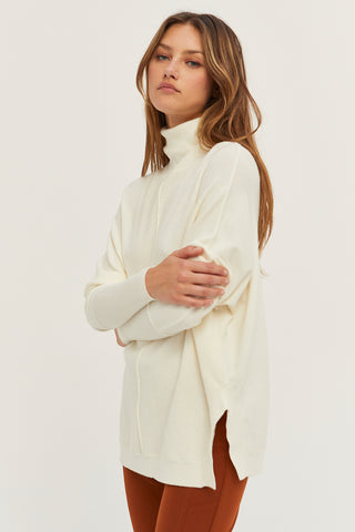 A model wearing a cream dolman sleeve sweater.