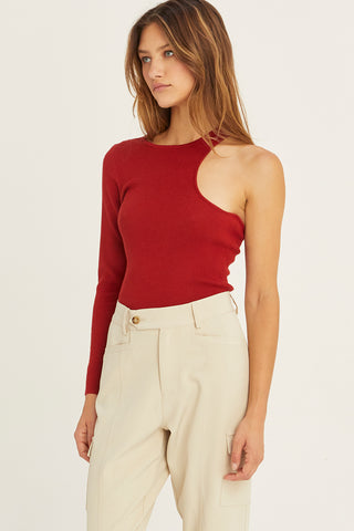 A woman wearing a brick one shoulder cut out sweater top.