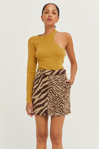A woman wearing a marigold one shoulder cut out sweater top.