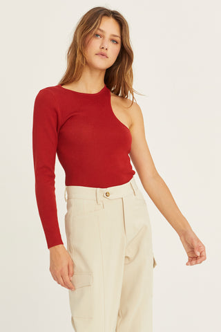 A woman wearing a brick one shoulder cut out sweater top.