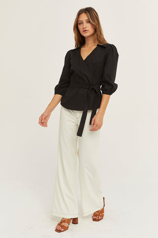 A woman wearing a black tencel wrap top.