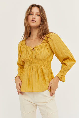 A woman wearing a marigold baby doll long sleeve top.