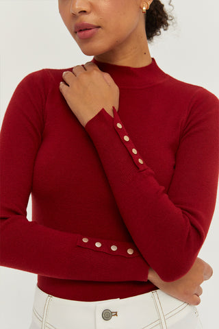 A woman wearing a red knit top with sleeve gold snap button detail.