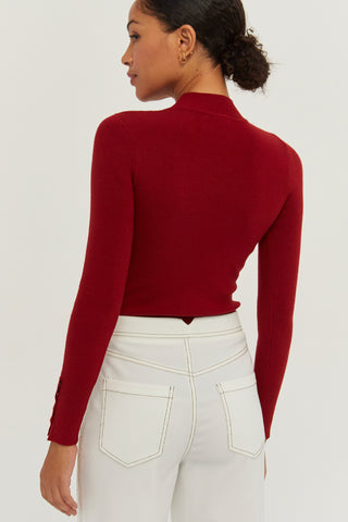 A woman wearing a red knit top with sleeve gold snap button detail.